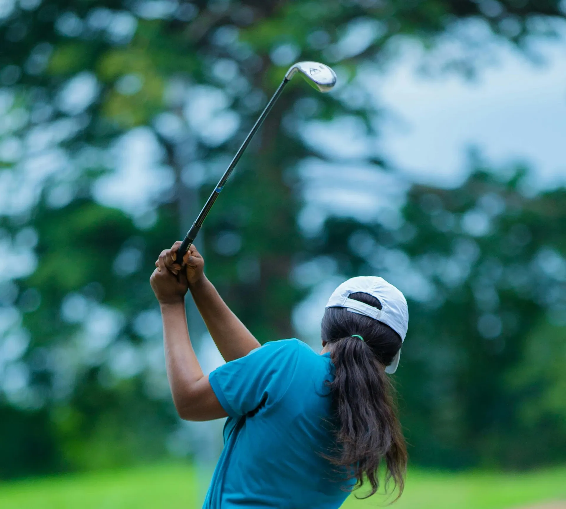 woman in hat swinging golf club outdoors on golf course