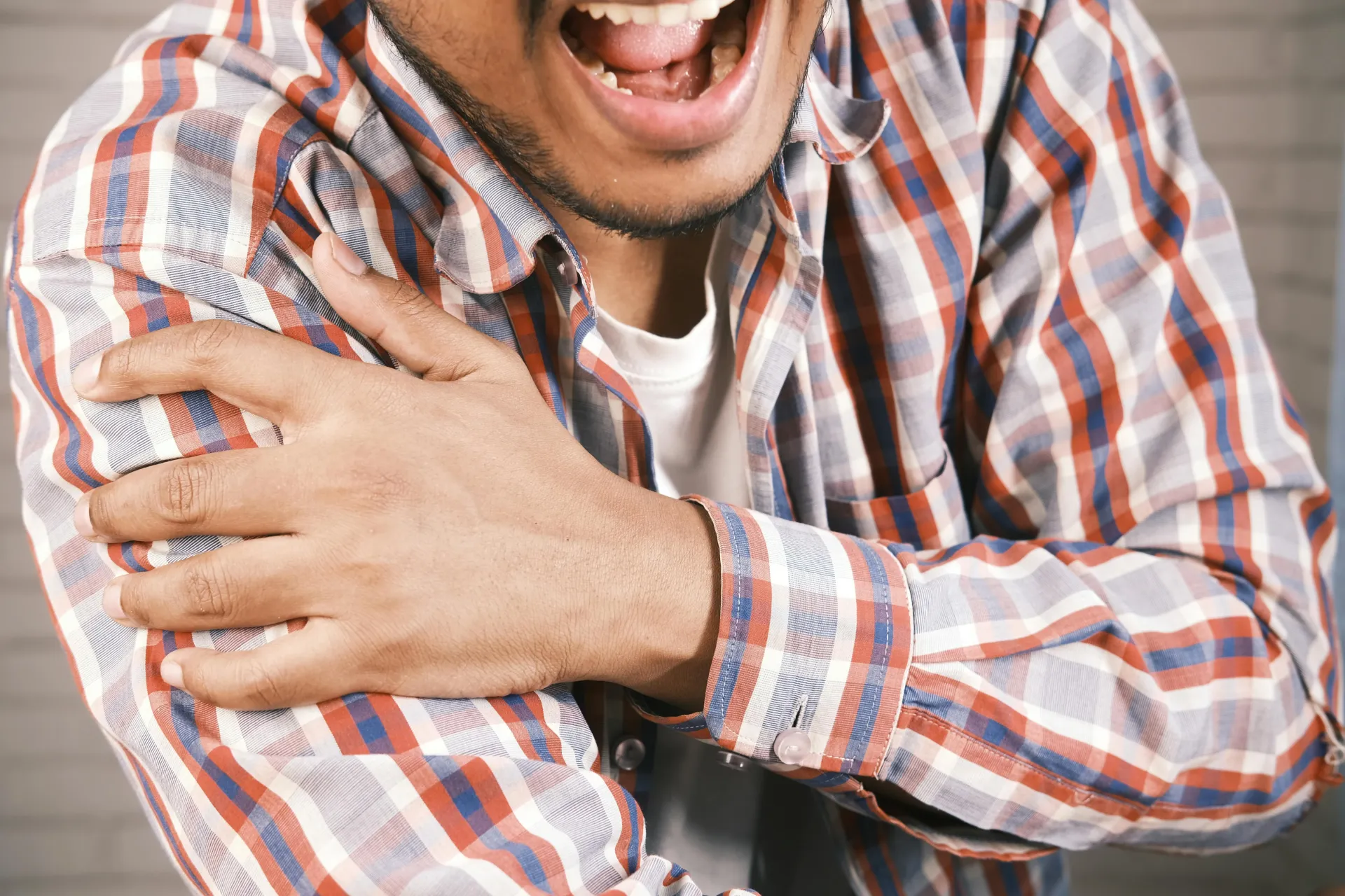 man in plaid shirt grabbing shoulder in pain
